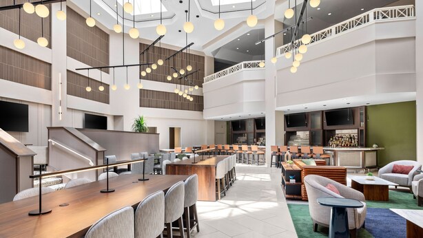 A spacious hotel lobby with a long reception desk, multiple seating areas, and a staircase leading to an upper level. - Sheraton Suites Galleria-Atlanta (Atlanta)