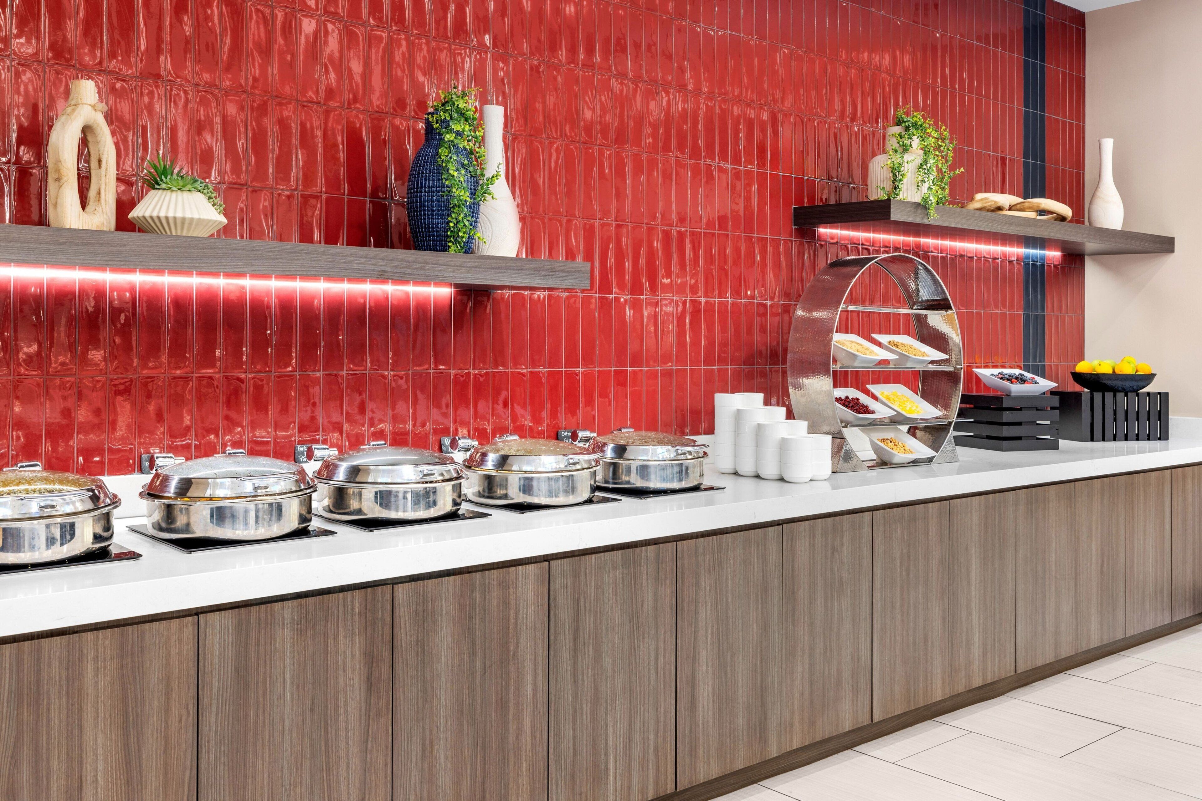 Ein reichhaltiges Buffet mit mehreren Servierstationen, einer roten Fliesenwand und verschiedenen Speisen, die auf Regalen und Theken präsentiert werden.