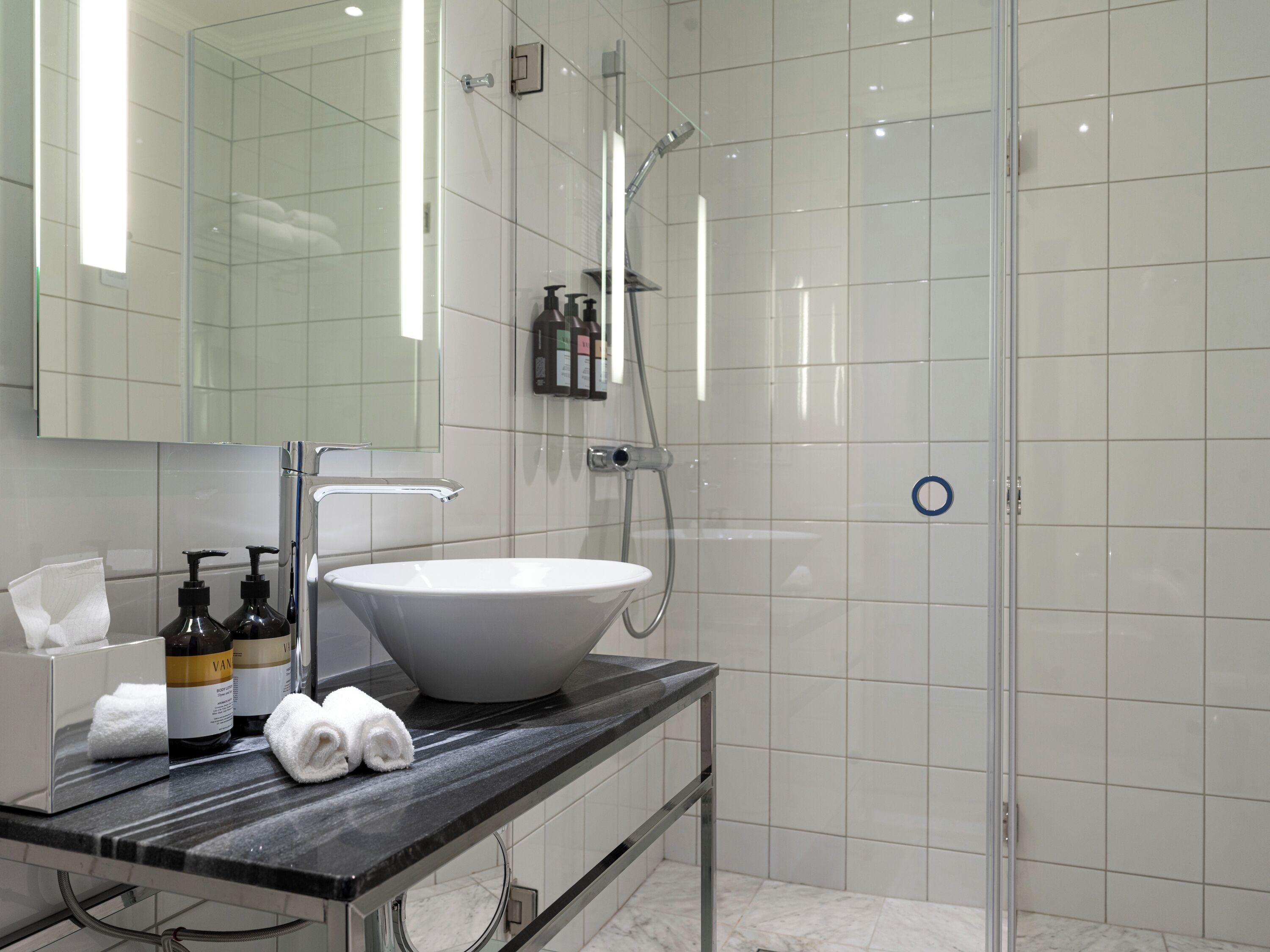 A modern bathroom with a large white sink, a mirror, and a glass shower enclosure.