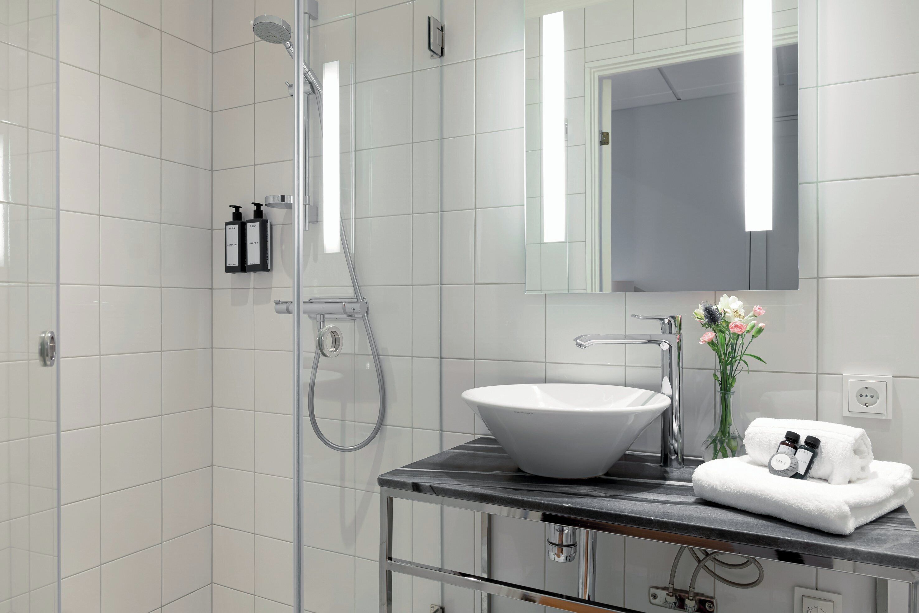 Un baño moderno con un lavamanos blanco, una cabina de ducha de vidrio y un espejo sobre el lavamanos.