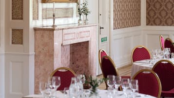 A dining area with marble fireplace, red upholstered chairs, and a white table set with wine glasses and cutlery.