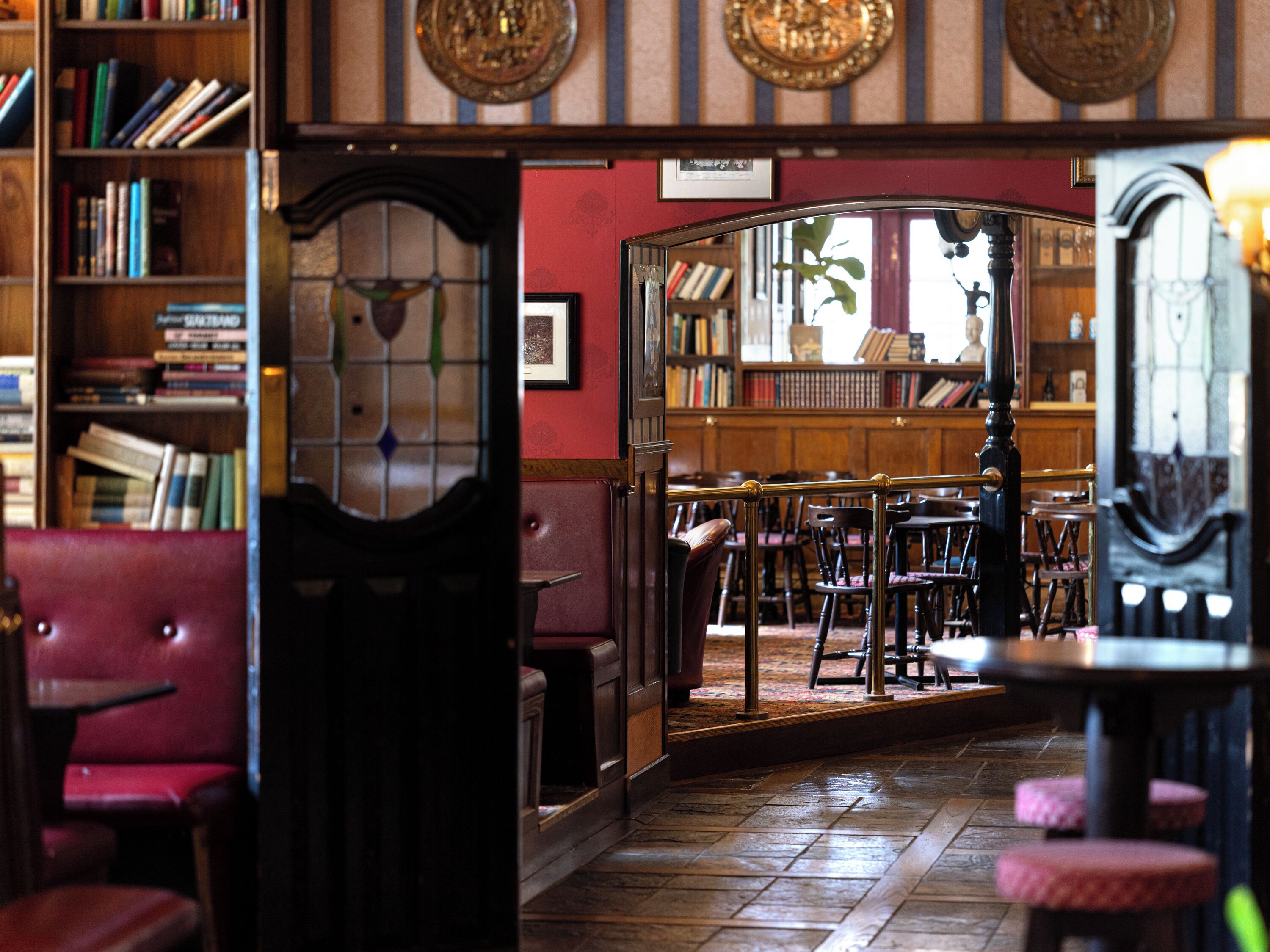 A library with bookshelves, a reading area with chairs, and a wooden floor.