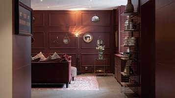 A room with a dark red wall, a red sofa, a small table with a vase, and a shelf with decorative items.