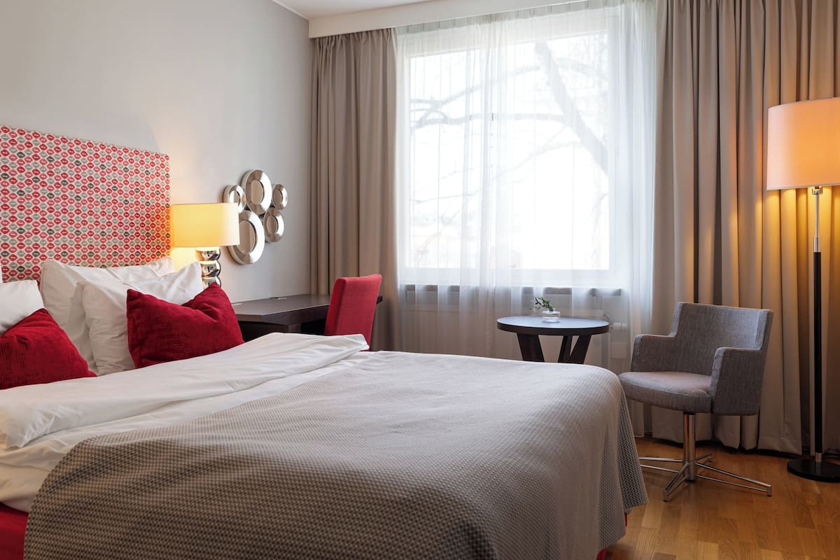 Ein Hotelzimmer mit einem großen Bett, einem Schreibtisch, einem Stuhl und einem Fenster mit Vorhängen.
