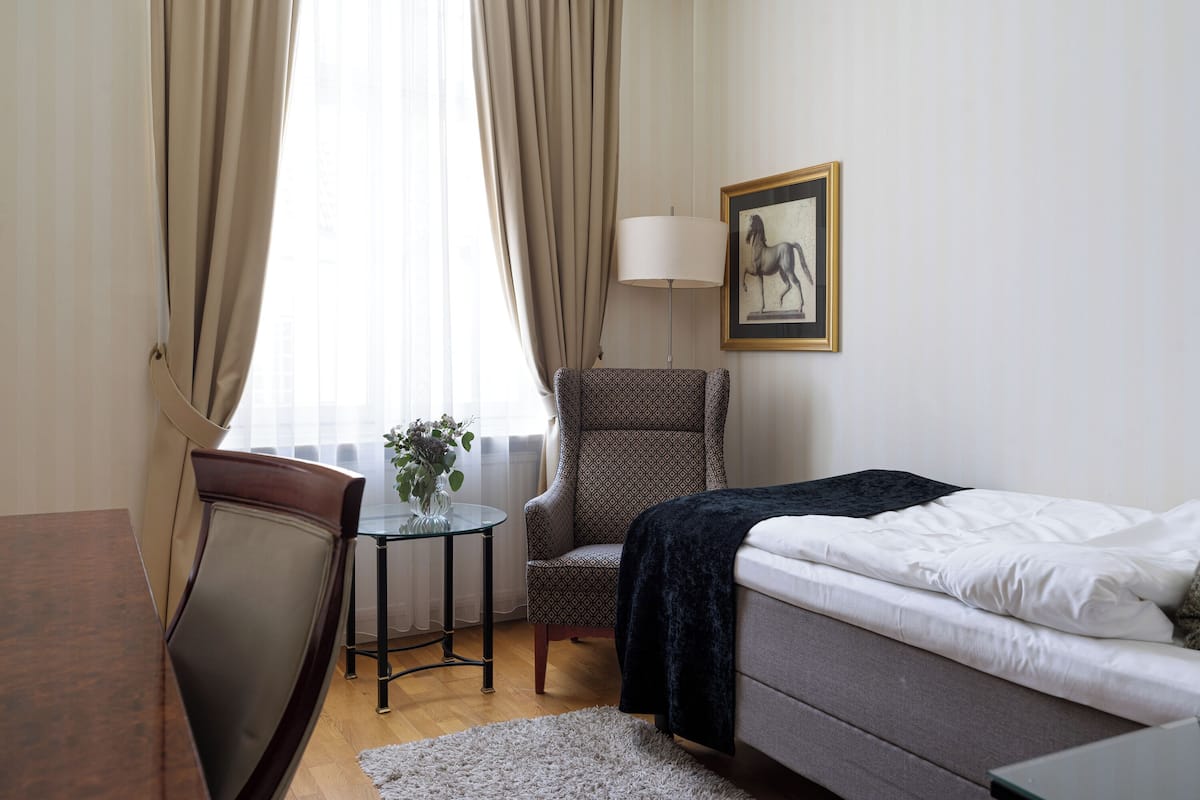 Ein Hotelzimmer mit einem Bett, einem Sessel, einem kleinen Tisch mit einer Vase und einer Lampe.