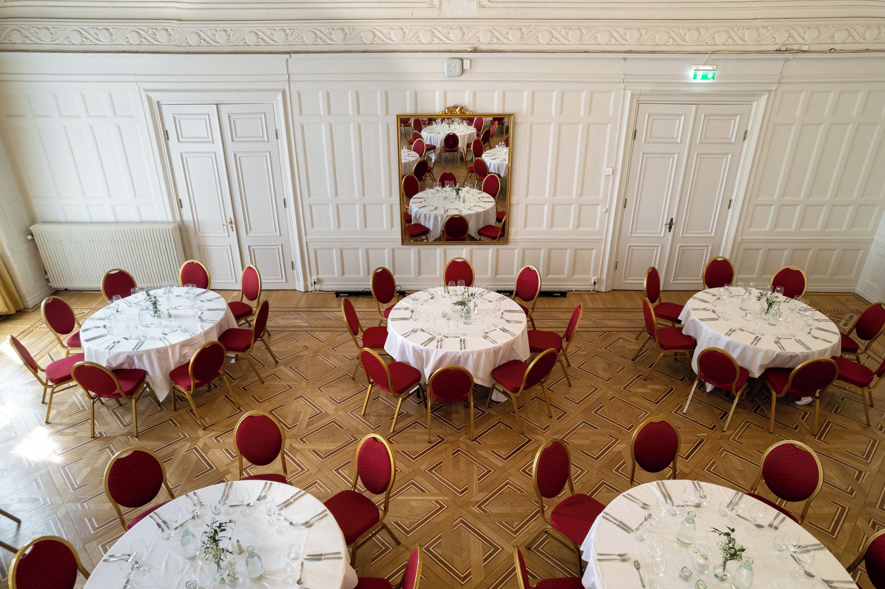 A banquet hall with multiple round tables, each set with white tablecloths and red chairs.