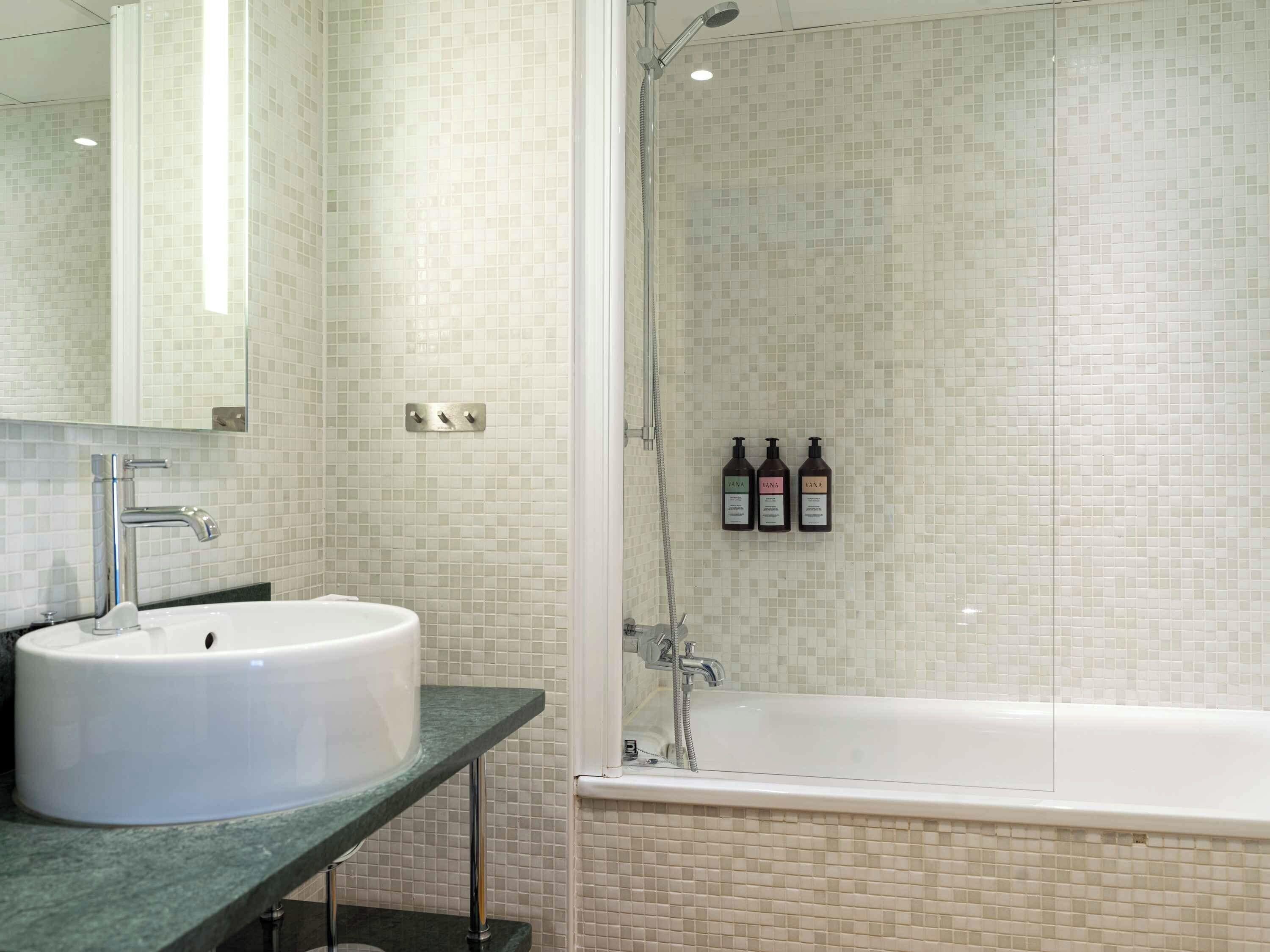 A bathroom with a white sink, a mirror, a shower with a glass door, and three bottles of shampoo on the wall.