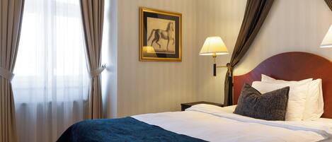 Habitación de hotel con cama, mesita de noche, lámpara, un cuadro en la pared y cortinas.