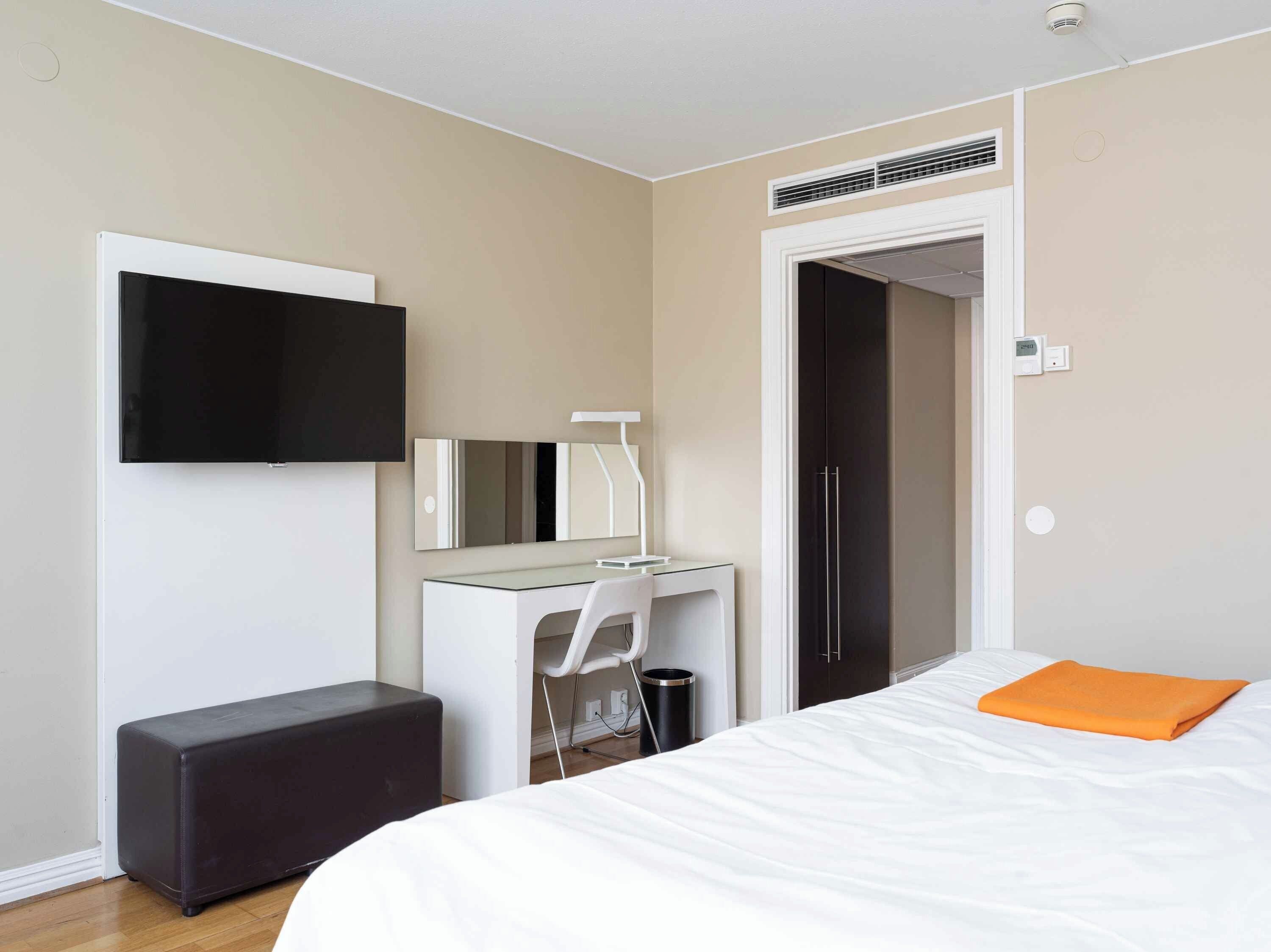 Ett modernt hotellrum med en säng, ett skrivbord, en stol, en tv och en garderob.