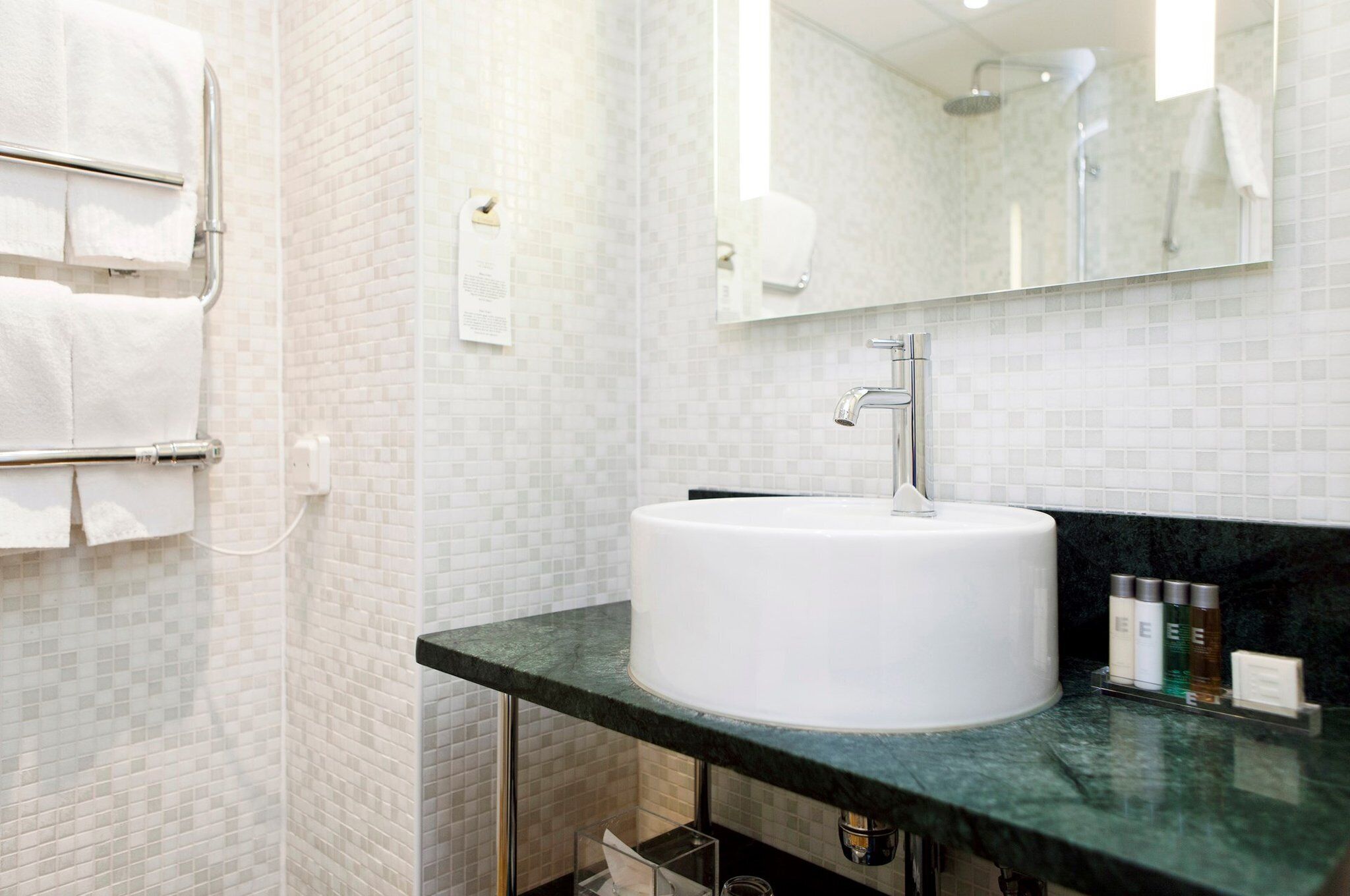 Un baño con un lavamanos blanco, un espejo y un perchero para toallas.