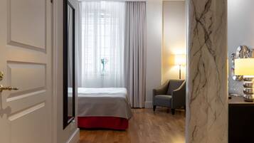 Habitació d'hotel amb un llit, una cadira, una columna de marbre i una finestra amb cortines.