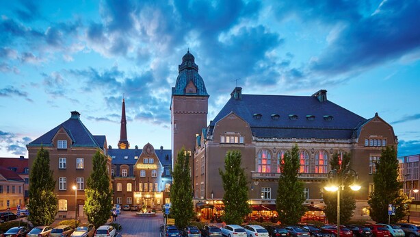 A historic building with a prominent tower and a large central structure, surrounded by trees and parked cars. - Elite Stadshotellet Västerås (Vasteras)