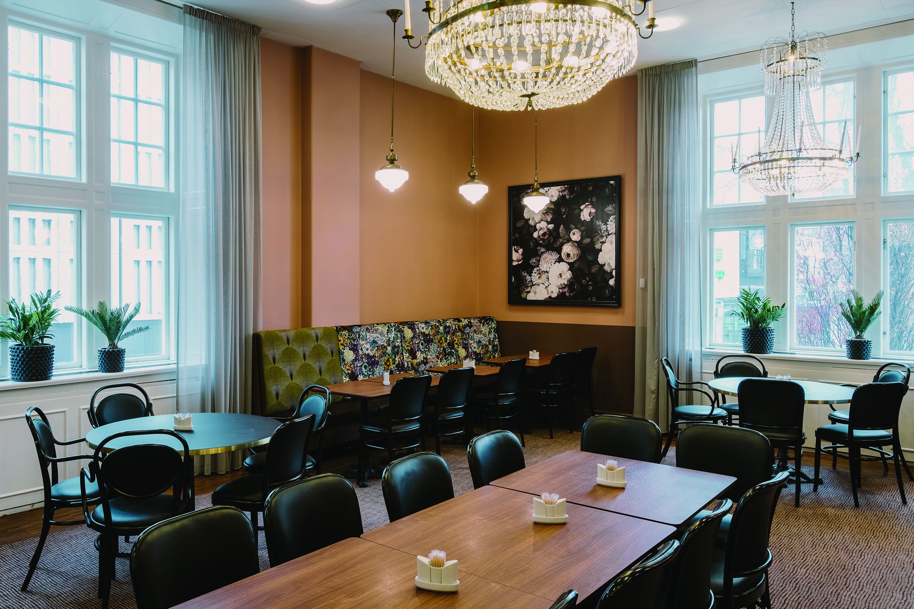 A conference room with a wooden table, black chairs, a chandelier, and a floral painting on the wall.