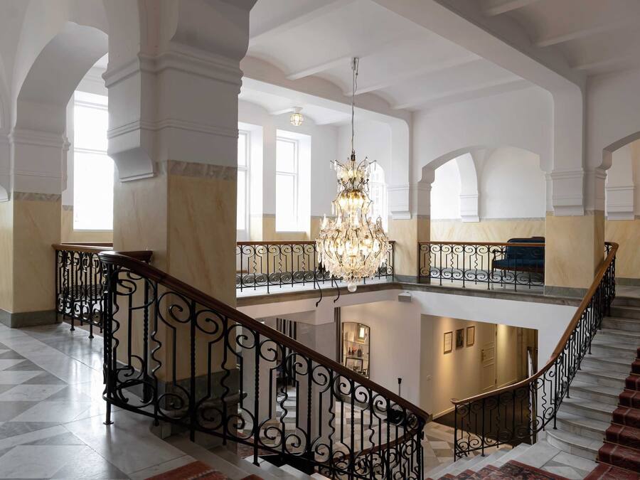 Ein prachtvoller Innenraum mit einem zentralen, offenen Bereich, einer Kristallleuchter und einer Treppe mit aufwendiger Geländerarbeiten.
