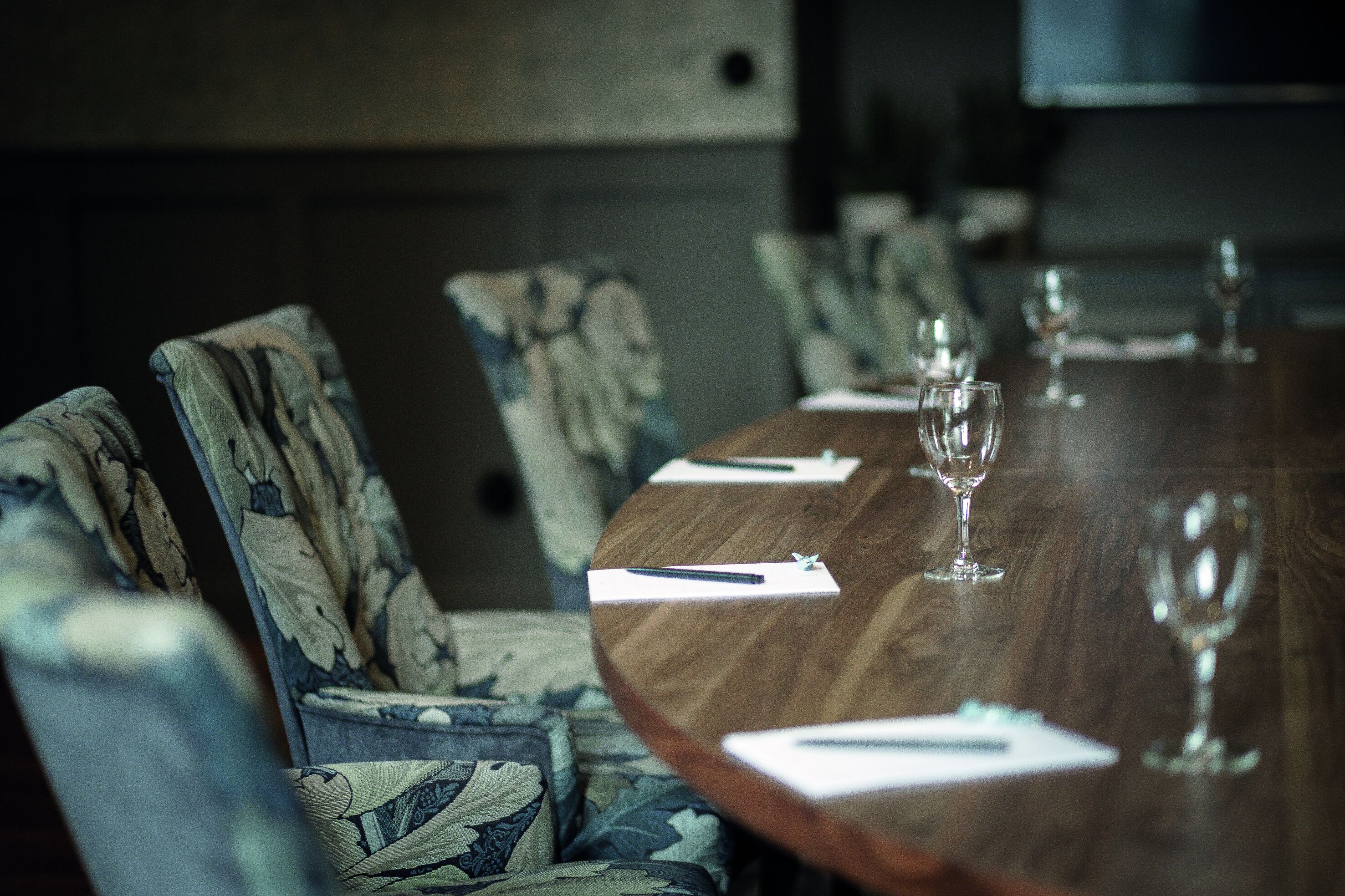 Une table de conférence avec des chaises, un plateau en bois et des verres à vin vides.