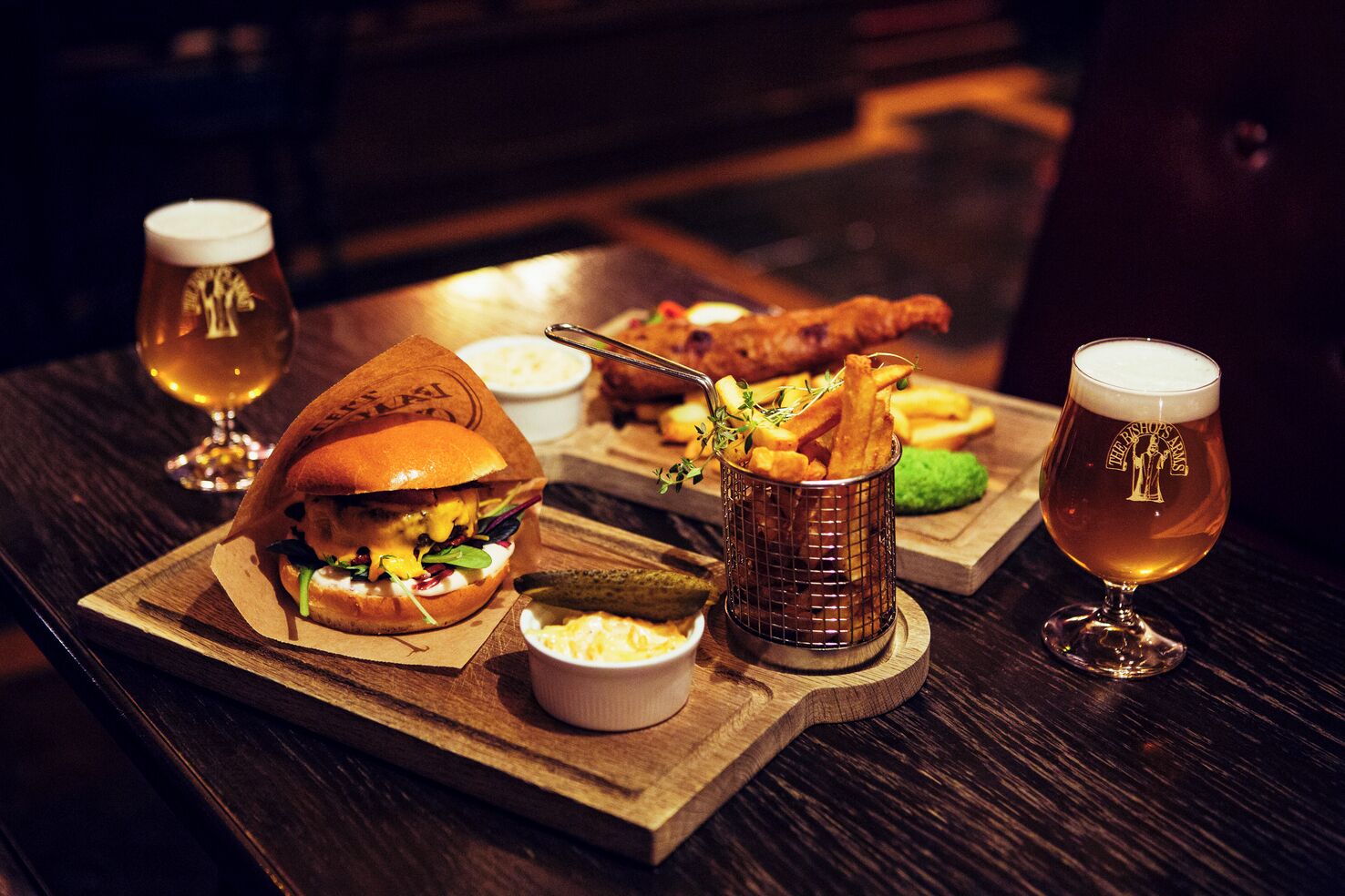 A meal tray with a burger, fries, a fish, and a drink on a wooden table.
