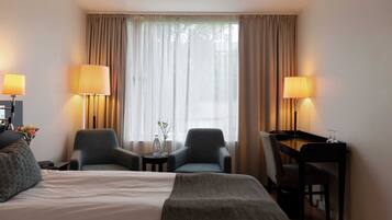 A hotel room with a bed, two armchairs, a desk, and lamps.