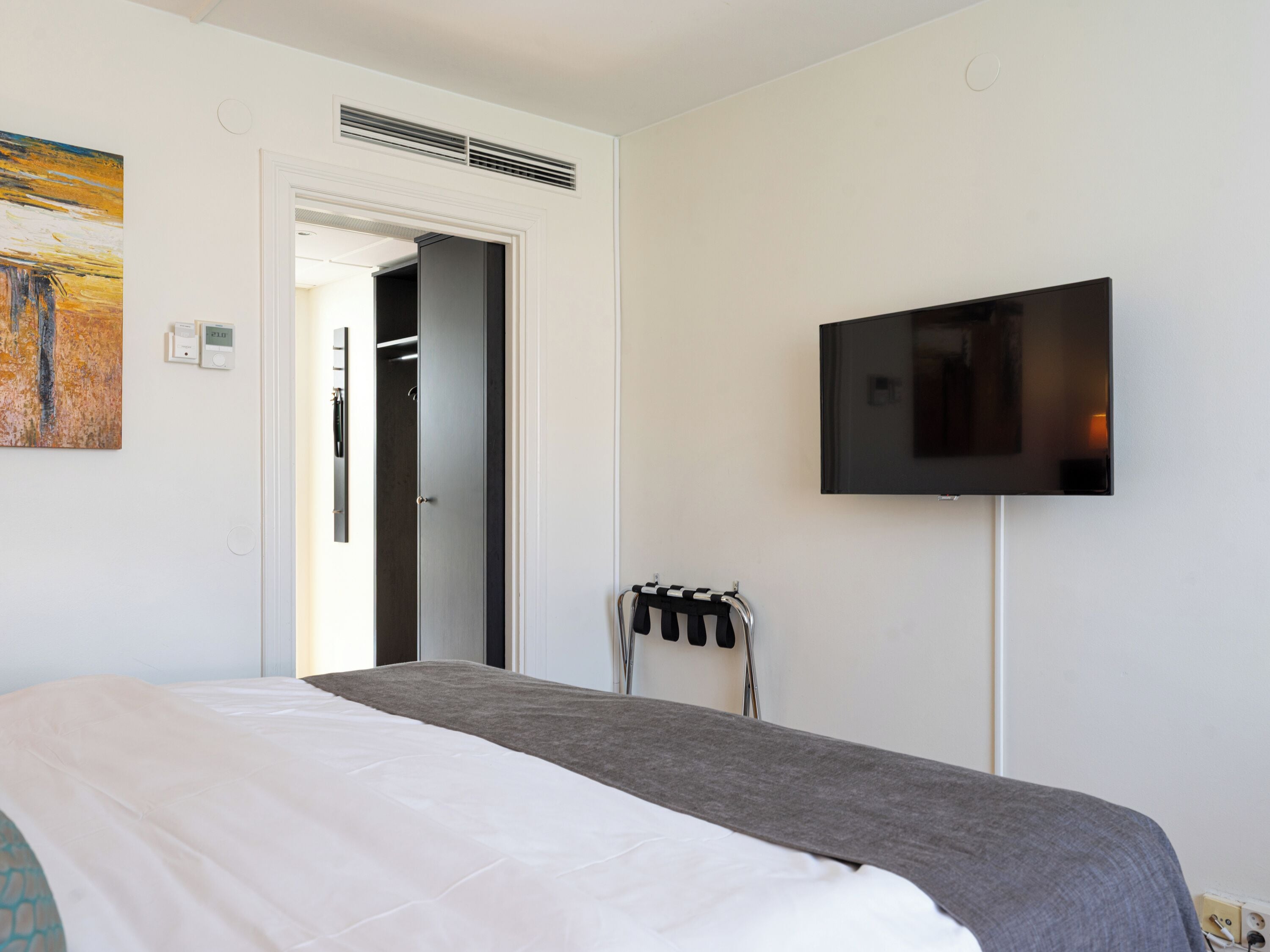 Een hotelkamer met een bed, een televisie, een schilderij en een deur naar een kast.