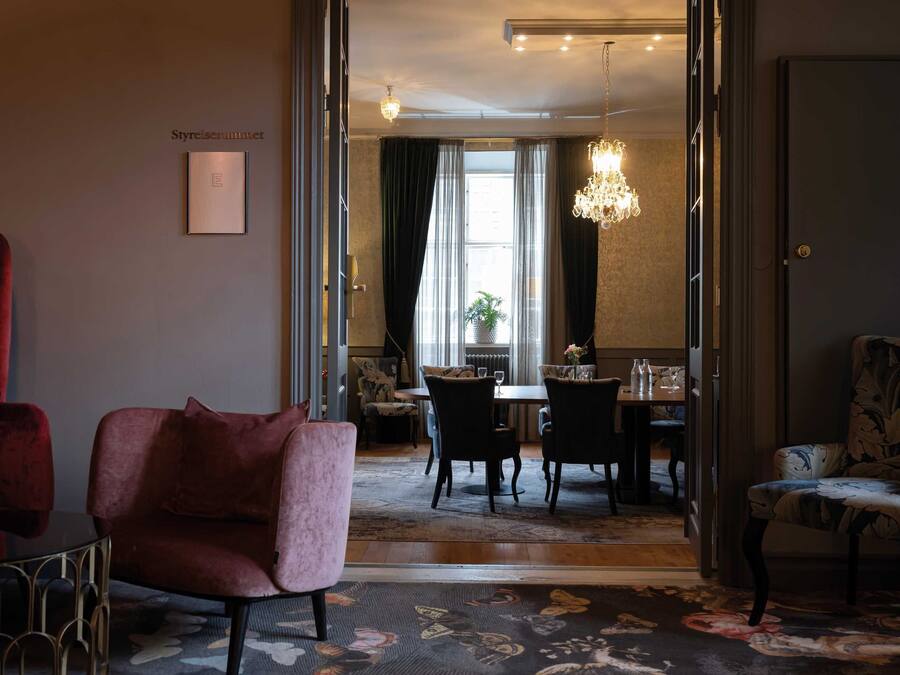 A hotel room with a dining area, a red chair, a patterned rug, and a chandelier.