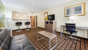 A hotel room with a sofa, a desk, a TV, a lamp, and a patterned floor. - Quality Inn Lincoln Cornhusker (Lincoln)
