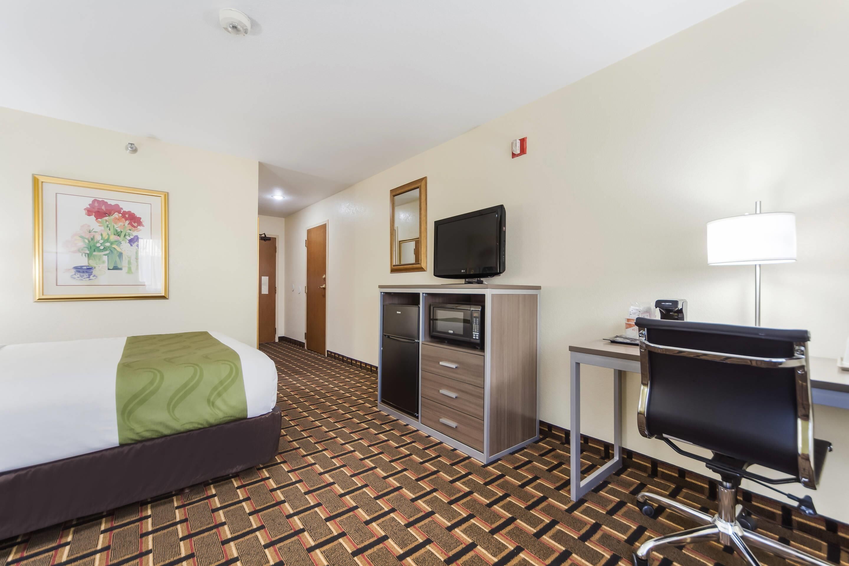 Een hotelkamer met een bed, een bureau met een computer, een televisie en een kast.