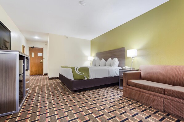 A hotel room with a bed, a sofa, a desk, and a lamp. - Quality Inn Lincoln Cornhusker (Lincoln)