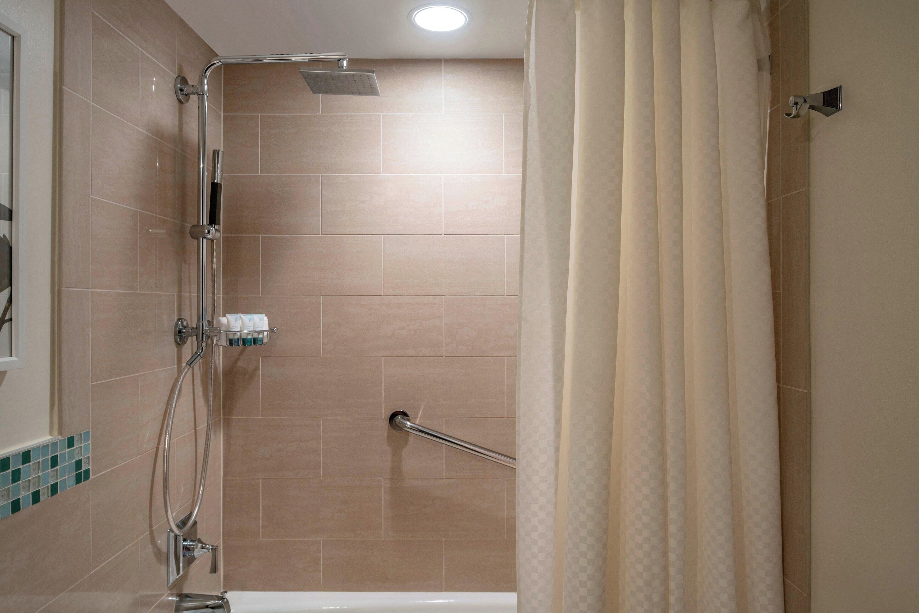 A shower area with a handheld showerhead, a glass-enclosed shower stall, and a towel rack with toiletries.