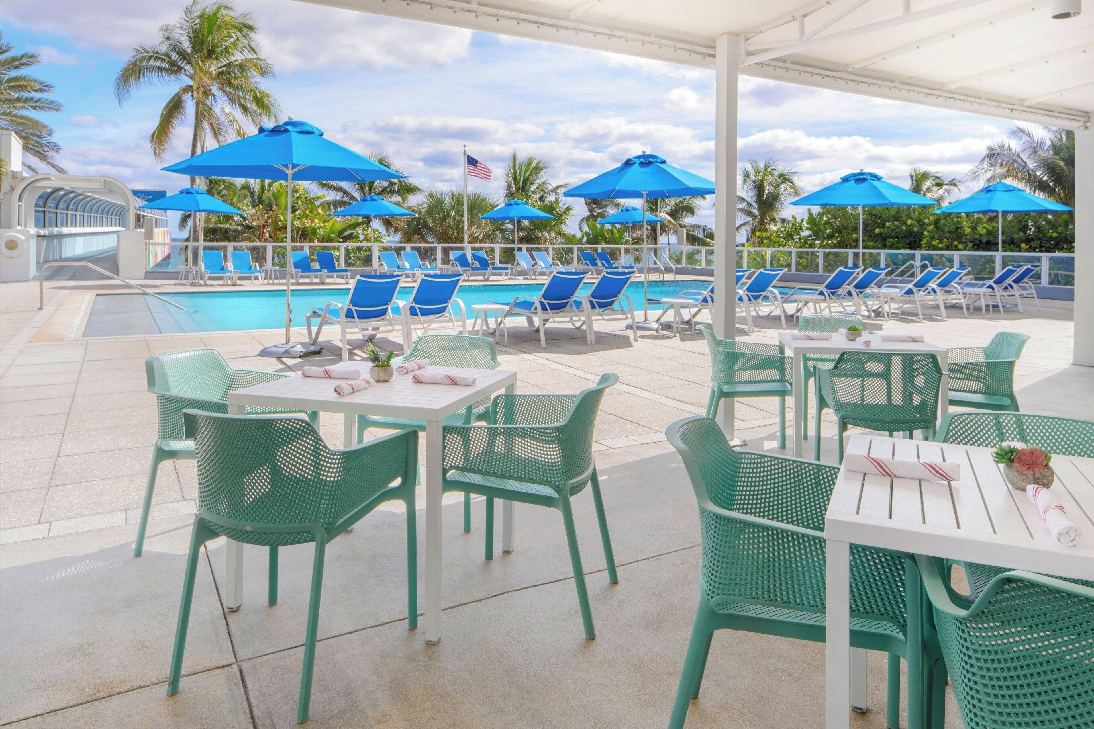A poolside area with lounge chairs and umbrellas, a pool, and a covered seating area with tables and chairs.