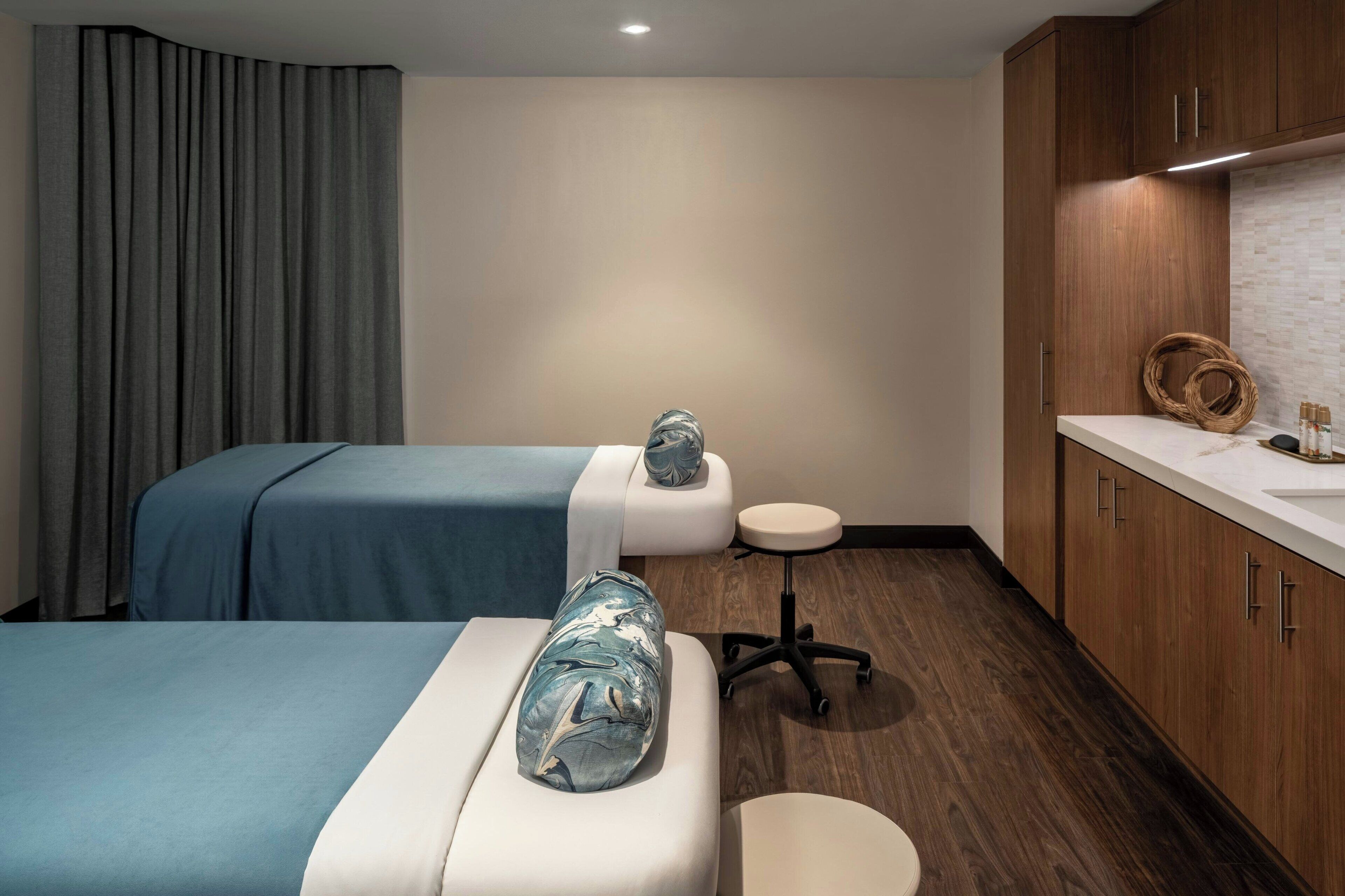 A hotel room with two beds, a small round table, wooden cabinets, and a white countertop.