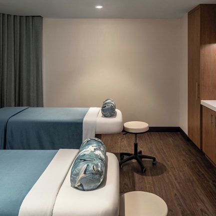 A hotel room with two beds, a small round table, wooden cabinets, and a white countertop.