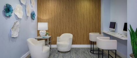 A modern reception area with a wooden panel wall, white chairs, a small table with a lamp, and a plant.