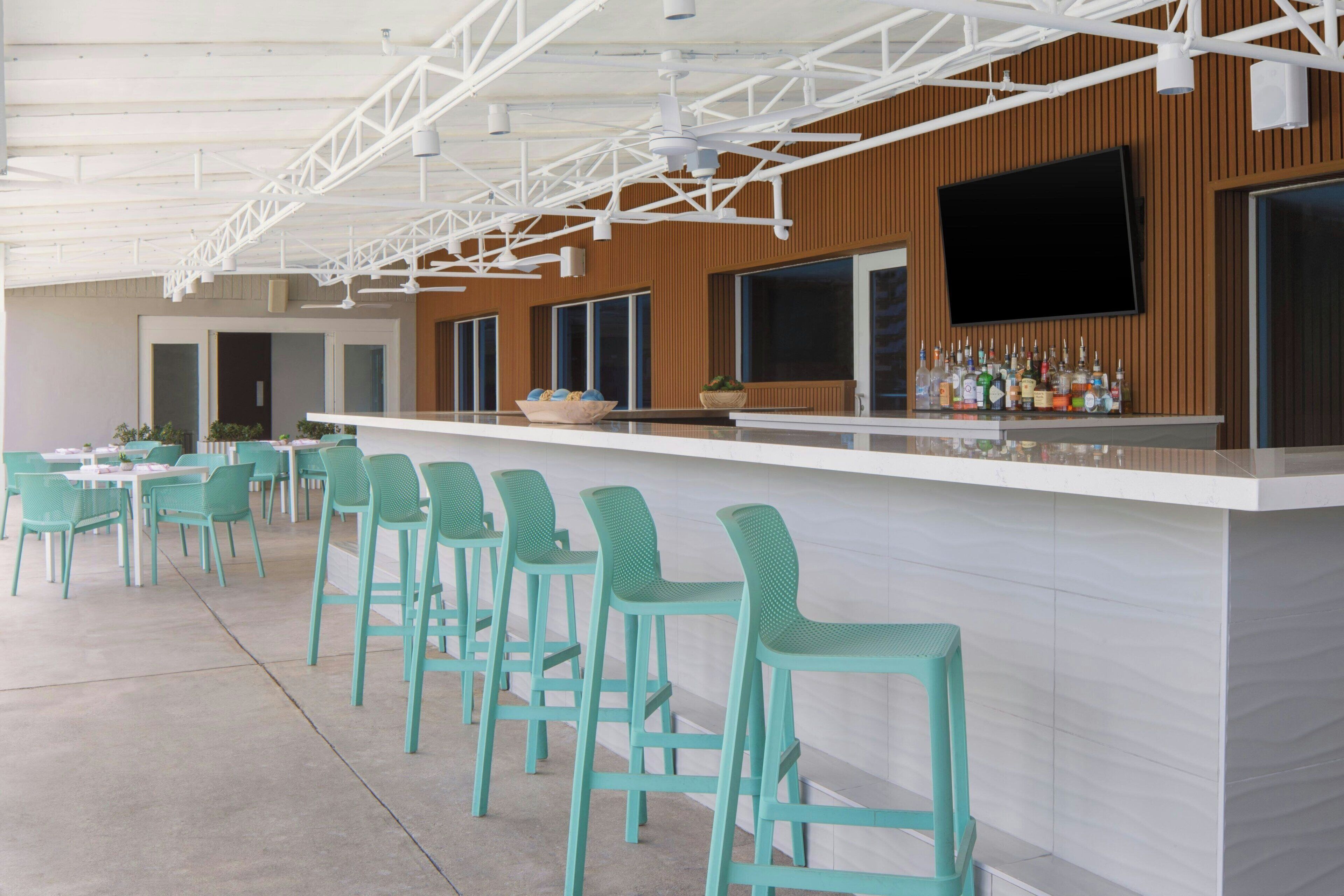 A bar area with teal chairs and a white counter, featuring a TV and various bottles.