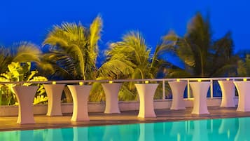 Zona junto a la piscina con pilares blancos y una piscina cristalina que refleja el cielo.