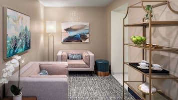 Ein modernes Hotelzimmer mit einem grauen Sofa, einem kleinen runden Tisch mit einem Orchideenstrauß, einer Stehlampe und einem goldenen Metallregal mit Teeservice.