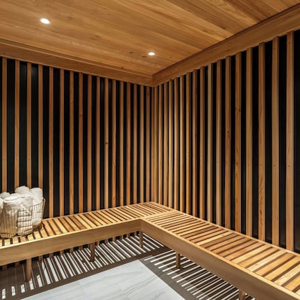 A wooden bench with a woven basket of towels in a room with vertical wooden slats on the walls and a ceiling with recessed lighting.