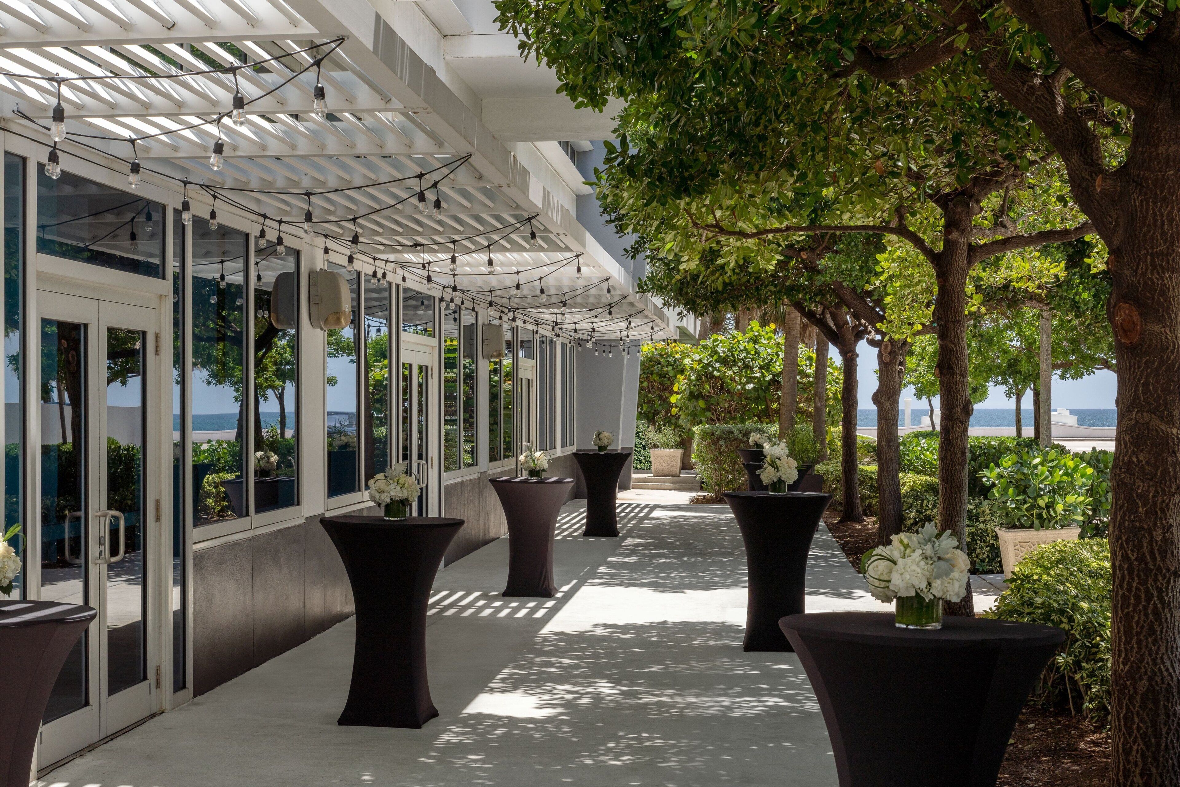 A covered outdoor corridor with large potted plants and a view of the sea.