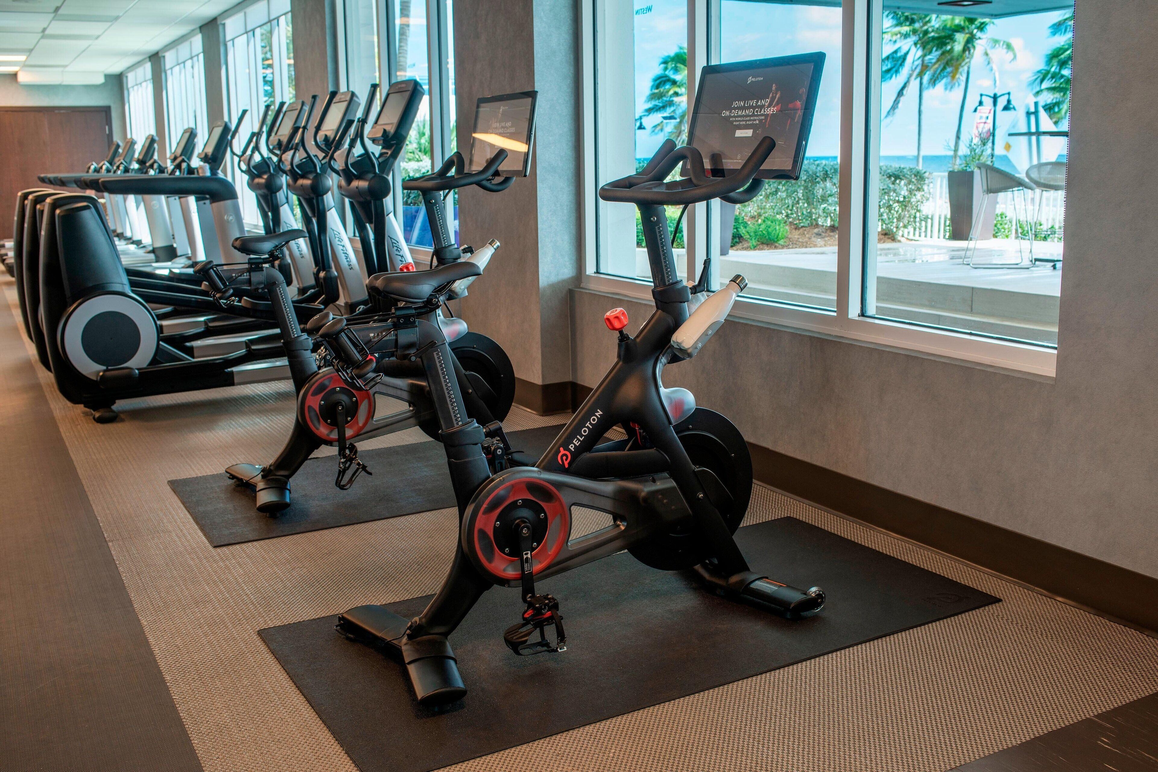 A gym with stationary bikes and treadmills, large windows, and a view of the outdoors.