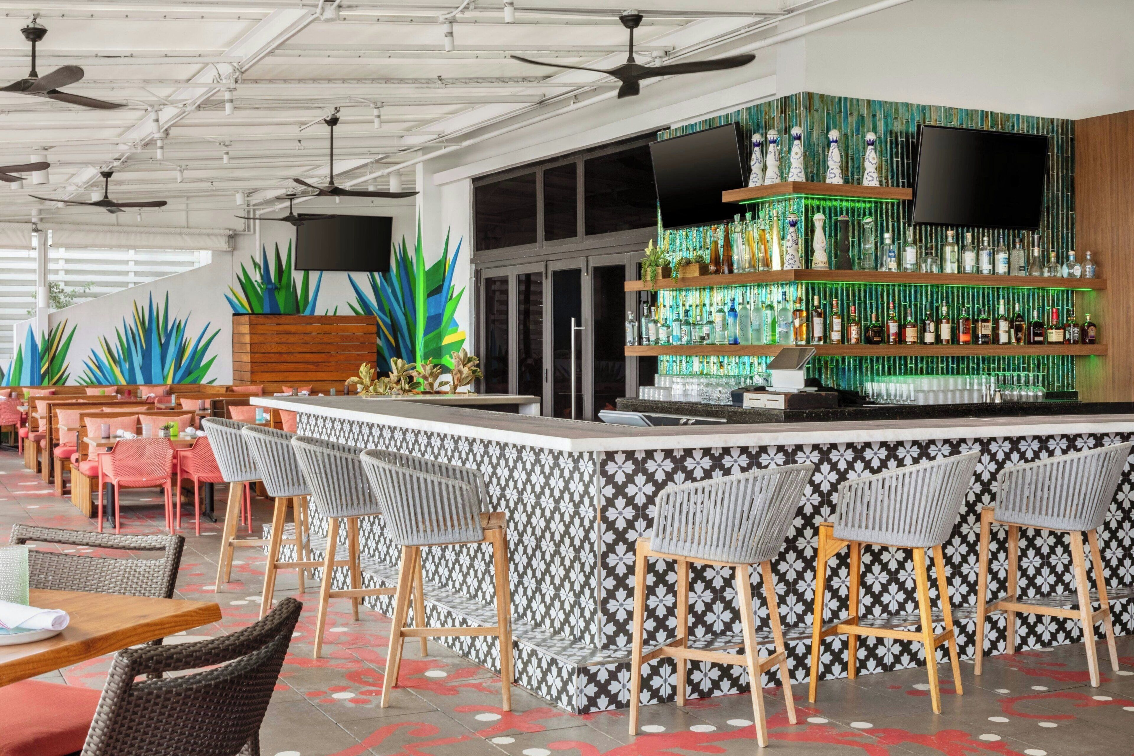 Zona de bar amb mostrador, tamborets i diverses ampolles.