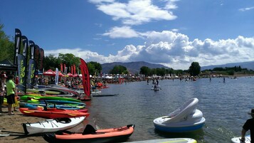 Evento a orillas del lago con varias canoas y tablas de remo, tiendas de campaña y una multitud de personas.