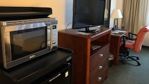 A hotel room with a microwave, a flat-screen TV, a wooden desk, a chair, and a lamp.