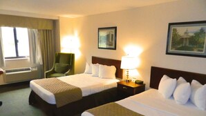 A hotel room with two beds, a chair, a nightstand with a lamp, and a window with curtains.