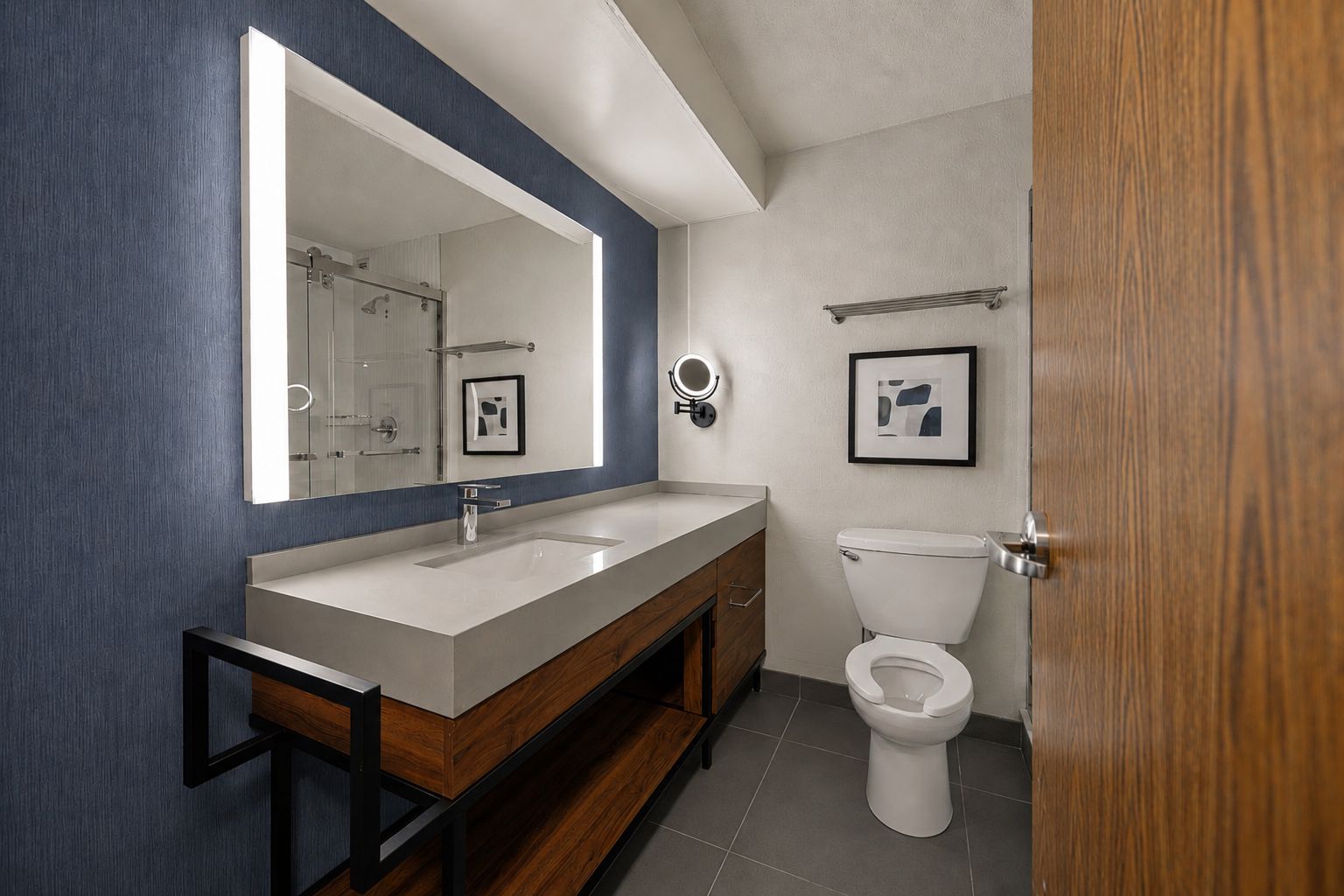 A modern bathroom with a large mirror, a sink, a toilet, and a framed picture on the wall.