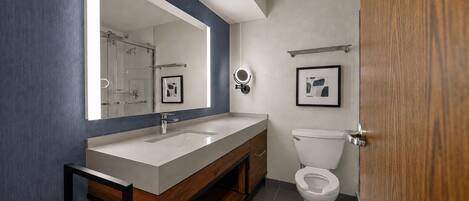 A modern bathroom with a large mirror, a sink, a toilet, and a framed picture on the wall.