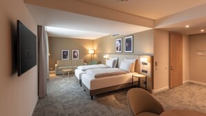 A hotel room with a large bed, two bedside tables, a flat-screen TV mounted on the wall, a sofa, a small table, and a door. - Mercure Parkhotel Mönchengladbach (Moenchengladbach)