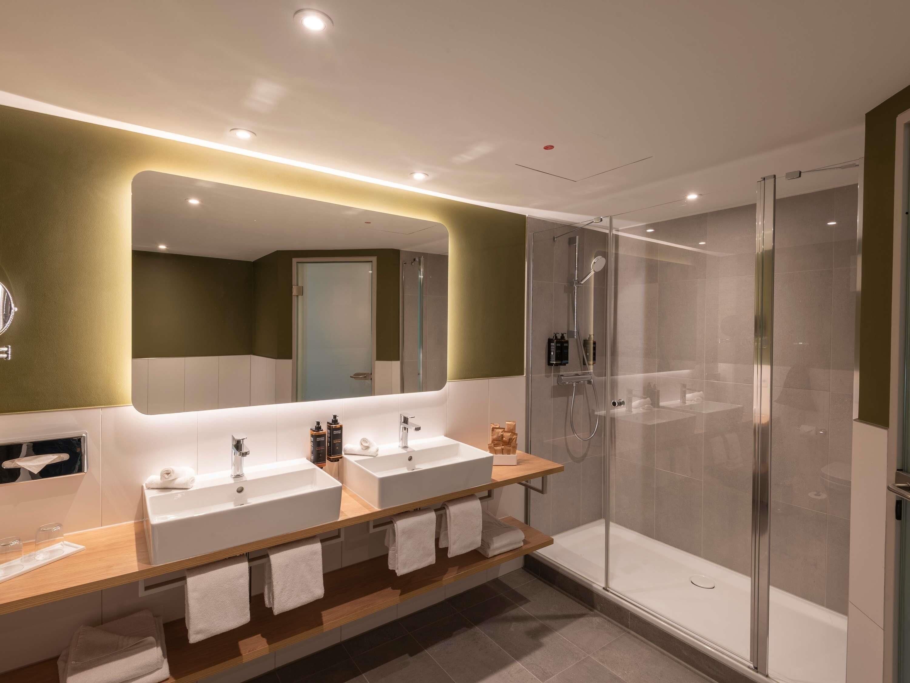 A modern bathroom with two sinks, a glass shower enclosure, and a mirror with integrated lighting.
