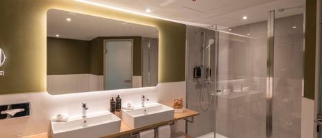 A modern bathroom with two sinks, a glass shower enclosure, and a mirror with integrated lighting.