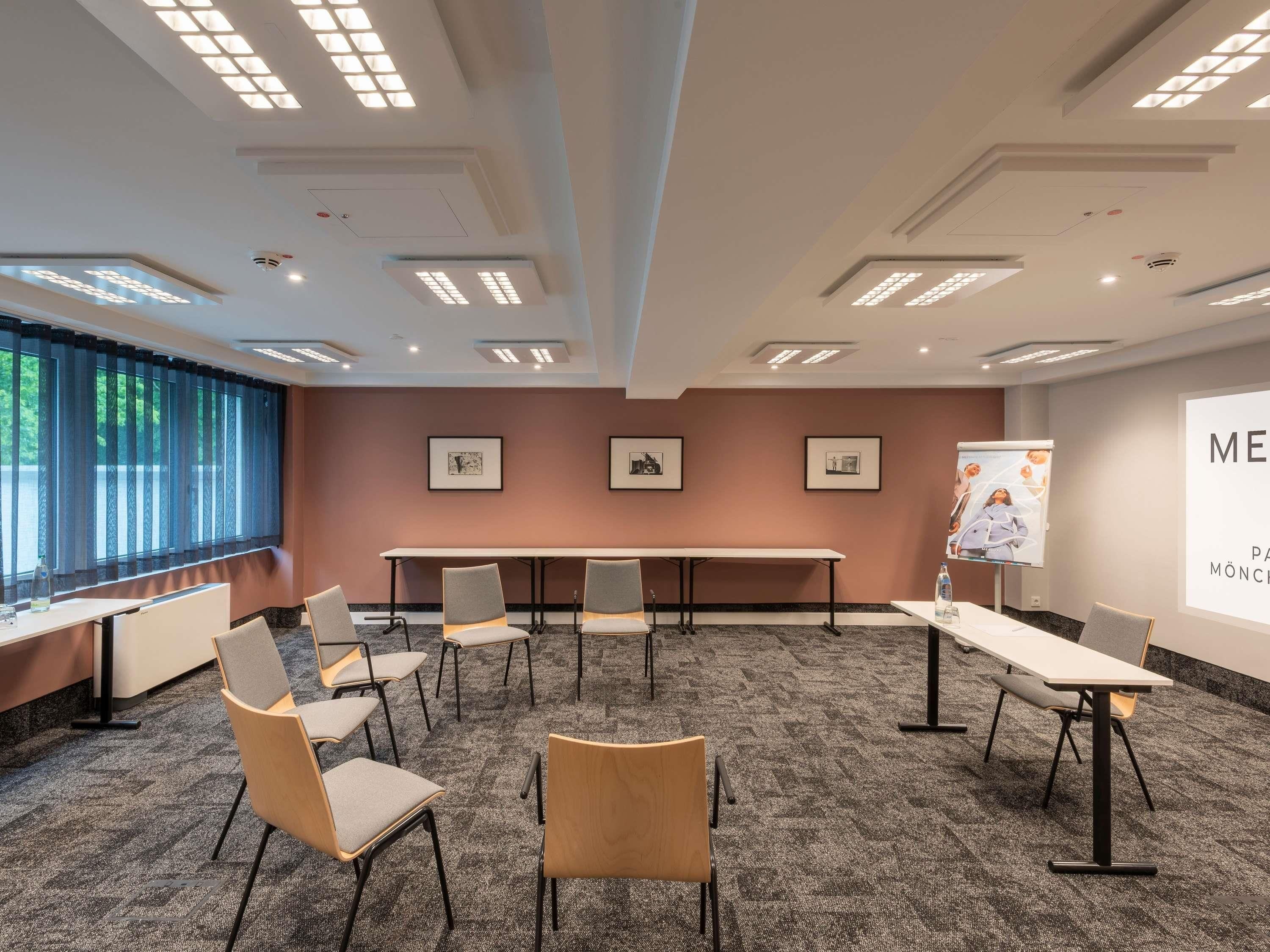 Un salón de conferencias con una larga mesa, varias sillas, luces en el techo, cuadros en la pared y una pantalla de proyección.