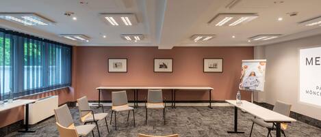 Un salón de conferencias con una larga mesa, varias sillas, luces en el techo, cuadros en la pared y una pantalla de proyección.