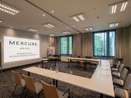 Una sala de conferencias con una pantalla grande mostrando 'MERCURE HOTEL PARKHOTEL MÖNCHENGLADBACH' al frente.
