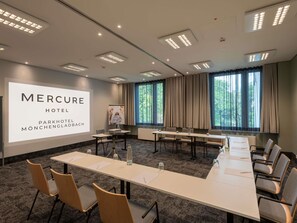 Ein Konferenzraum mit einer großen Leinwand, auf der 'MERCURE HOTEL PARKHOTEL MÖNCHENGLADBACH' zu sehen ist.
